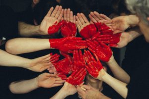Many hands in a mime-like position being painted with a red heart. Photo Credit: Tim Marshall on Unsplash